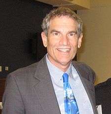A photo of Duane Silverstein wearing a grey suit and a blue tie.