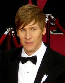 Profile of a man with medium brown hair at a red carpet event. He is seen wearing a white collared shirt and black tuxedo accented with a black bowtie.