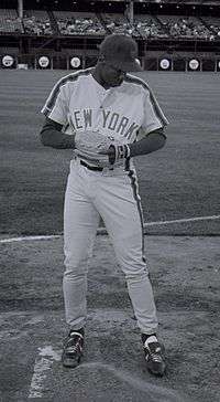 A man in a light baseball uniform with "New York" on the chest and a dark baseball cap.