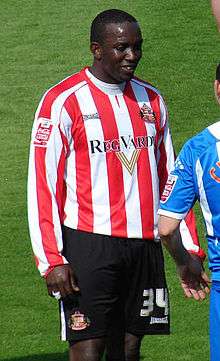 Dwight Yorke wearing a long-sleeved red-and-white-striped football jersey and white shorts with a number 34 on the left leg.