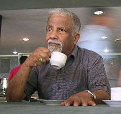 Old man drinking from a white cup in his hand.