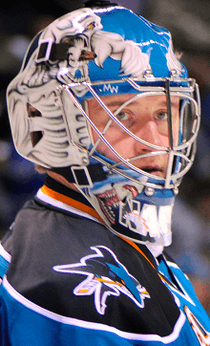 A side shot of an ice hockey player's head and shoulders. He is wearing a blue helmet and a black and blue uniform.