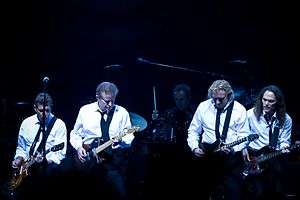 A color photograph of four members of the Eagles on stage with guitars