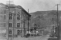 A partial black-and-white view of the Wheeler from a slightly different angle than that shown in the article's lead photograph, looking down the street towards a mountain in the distance. Telephone poles and wires run along both sides, and a small electric light is suspended above the intersection.