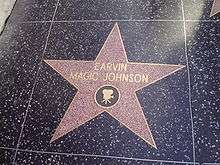 A five-point star engraved on a tile. In the center of the star are the words "EARVIN MAGIC JOHNSON". An image of a movie camera is etched directly below these words, though still in the star.