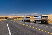 A truck traveling on a two-lane road surrounded by wheat fields
