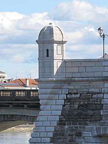 Photographie d'une échauguette de pierre blanche se détachant au-dessus d'un pont.