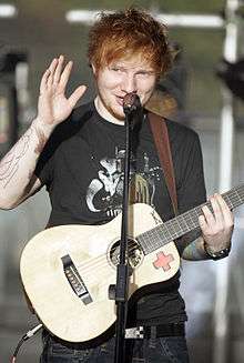 A man waving his hand and holding a guitar.