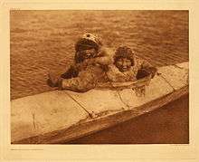 Photo of two males wearing fur sitting in well of large kayak
