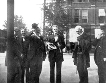 Black-and-white photograph of six men standing: All of them are well-dressed in suits and ties. Cope has short hair, mustache, and a small beard; in his hands he holds a wide-brimmed hat and some papers.
