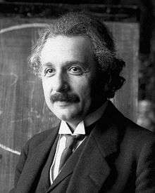 Head and shoulders photo of  Einstein with moustache and graying, curly hair, smiling slightly