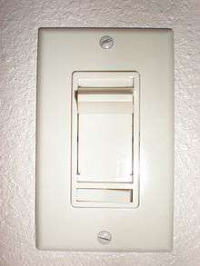  Vertical rectangular plastic cover plate with vertical slider and a smaller horizontal rocker switch below. Two exposed slotted screw heads hold the cover plate to the wall box.