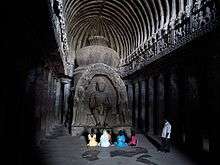 people sitting before stone shrine the Buddhist "Carpenter's Cave" at Ellora in Maharashtra, India