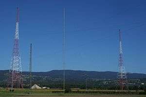Two metal-truss radio towers against a blue sky.