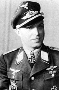 The up body of a man, shown from the front. He wears a peaked cap and a military uniform with various military decorations and an Iron Cross displayed at the front of his shirt collar. He is smiling; his eyes are looking to the left of the camera.