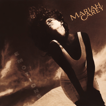 A brunette woman in a white dress standing in front of a dark desert like background, the words "MARIAH CAREY" are on the left hand side of the artwork with the words "EMOTIONS" are towards the bottom right hand side of the artwork.
