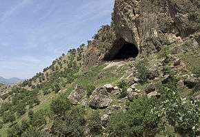 An entrance to a cave in a wooded hillside