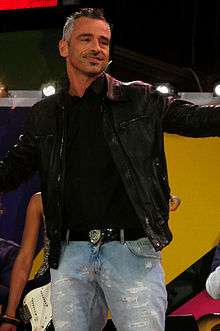 A man wearing a black leather jacket and blue jeans is performing