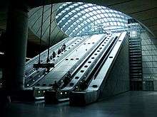 View of escalators rising up from the darkness of the station concourse to the brightness of the arched glazed roof over the entrance