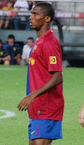 A black man wearing a blue-and-red halved shirt and blue shorts.