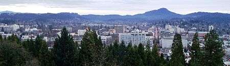 The flat-roofed buildings of downtown Eugene in front of Spencer Butte, a prominent forested hill
