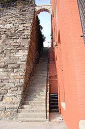A long steep staircase with a stone wall on the left and a painted red brick wall on the right.