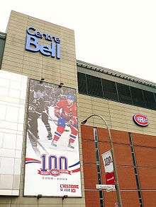 Façade of the Bell Centre. On the wall is a banner celebrating the Canadiens centennial, featuring two players, one in black and white and one in colour, and the Canadiens logo in front of a "100".