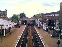 A view from a bridge down onto the railway tracks of Falkirk Grahamston Station. The main building on the left and a waiting room on the right side of the tracks with another road bridge in the distance