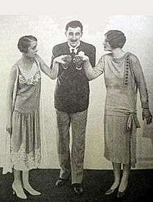 smart youngish man in blazer, kissing the hands of two youngish women either side of him