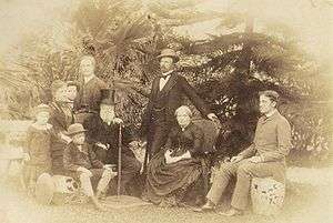 A group of figures surrounds the seated Emperor and Empress in this outdoor photograph.