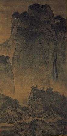 A long, portrait oriented scroll depicting a very tall mountain in the background and a stream with trees in the foreground, near the bottom of the painting. Contrary to the name of the painting, there are no travelers shown.