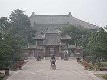 Several buildings are on an axis in front of one another, with the main hall at the end, partially obscured by the buildings in front.