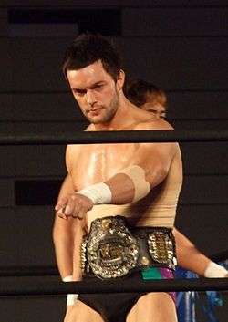 Prince Devitt with the IWGP Junior Heavyweight Championship belt in a wrestling ring