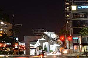 An elevated metro station at night with tall buildings on opposite sides.