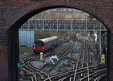 A view through a red-brick archway of a bridge. A complex of railway tracks interconnected with points is in the foreground with a train in the distance