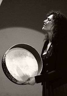 Young woman singing into a hand drum with her eyes closed