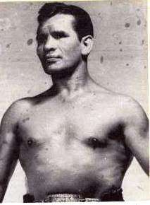 A black and white photo of a bare chested Mexican male with black hair.