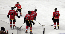 View from behind of five hockey players, each wearing red uniforms with black trim. The back of all five players reads "MCCRIMMON 4".