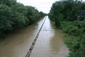 A divided highway with a metal guardrail in the middle completely covered in brown water during a rainstorm