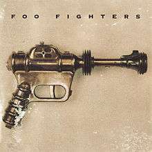 A toy of a futuristic pistol in front of a beige background. The title "Foo Fighters" is seen atop the toy.