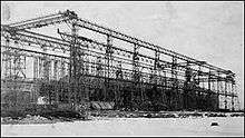 A ship's hull sits within the skeleton of a gantry crane