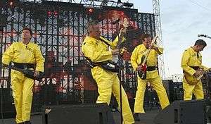 Devo onstage, wearing their trademark bright yellow costumes