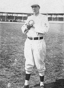 A man in a white baseball uniform with an overlapping "STL" on the left sleeve stands with his fists together wearing a glove on his left.