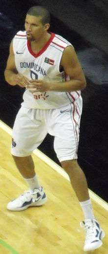 A man with a close-cut hairstyle, wearing a white basketball jersey, preparing to catch a pass