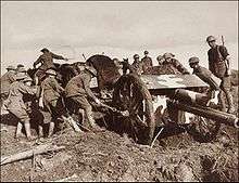 a collection of men pulling a field gun through the mud