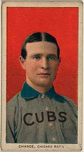A man with brown hair wearing a grey baseball uniform with a blue collar and the word "CUBS" on his chest in front of a red background