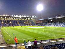 Fratton Park football stadium at night, home to Portsmouth F.C. The pitch is lit by floodlights.