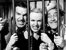 Fred MacMurray, Carole Lombard and Barrymore making funny faces behind prison bars; MacMurray and Lombard fiercely show their teeth, while Barrymore crosses his eyes goofily