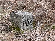 Square grey stone in scrubby brown grass with "DDR" carved on the right face.