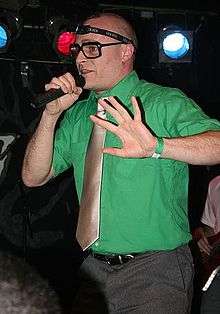 Photograph of a man in a green shirt holding a microphone.